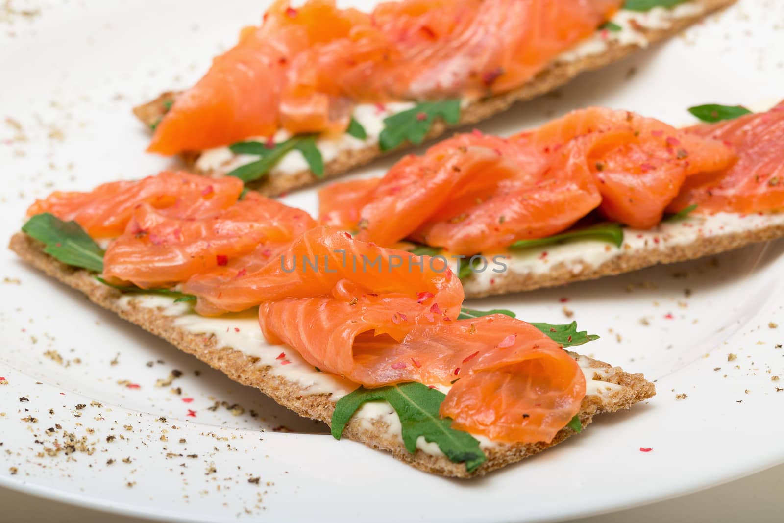 Salted salmon on crispy bread with cheese and arugula, closeup