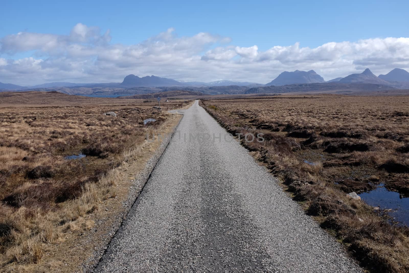 A tarmac single track road cuts through moorland towards the mountains on the horizon.