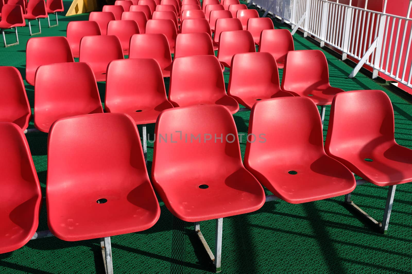 Rows of bright red plastic seating on a green rubber flooring.