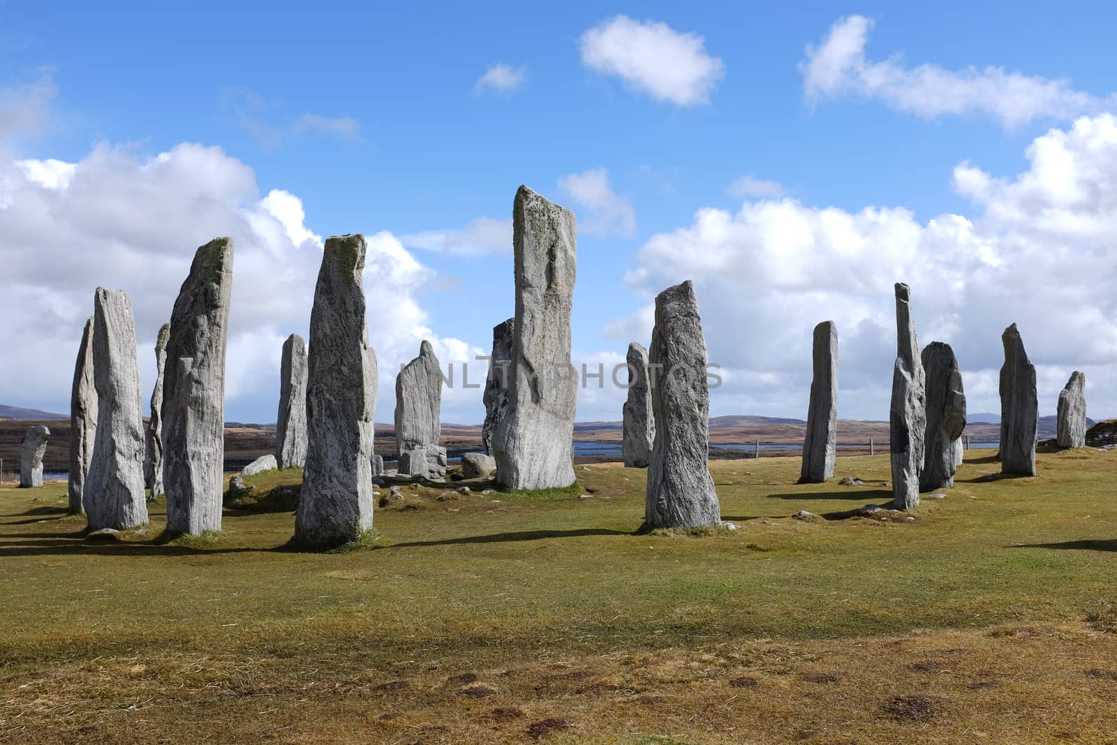 Standing stone circle on green grass with a blue cloudy sky at Callanish, Isle of Lewis, Scotland, UK.