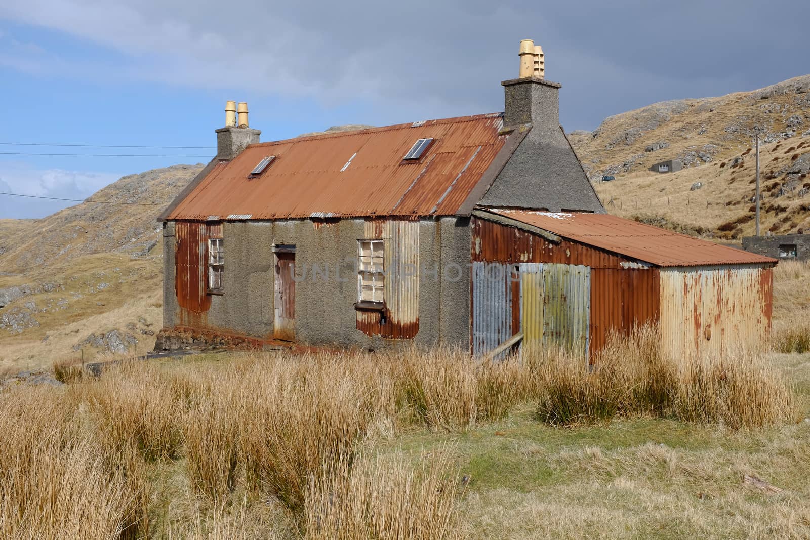 An old derelict building on moorland with tin corrugated roof and shed attached with partial render on the walls.