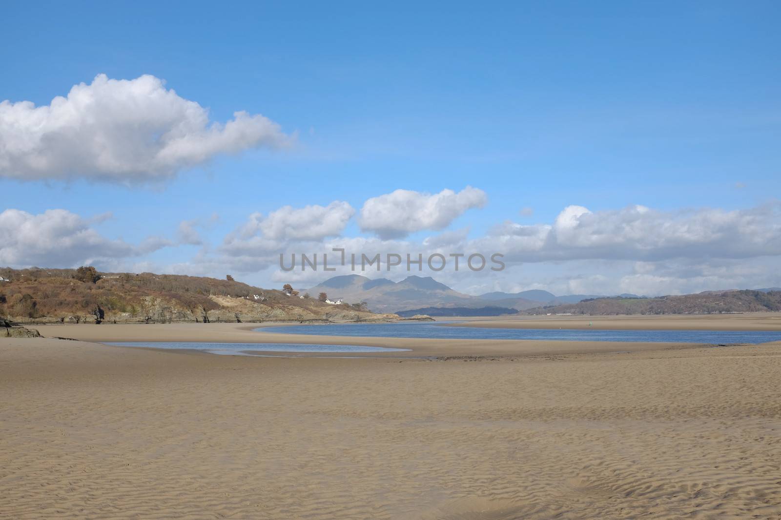 A deserted beach at low tide in an estuary at Borth y Gest, Gwynedd, Wales, UK, looking on to the Moelwyn mountain range, Snowdonia national park, Wales, with a big blue sky and white clouds.