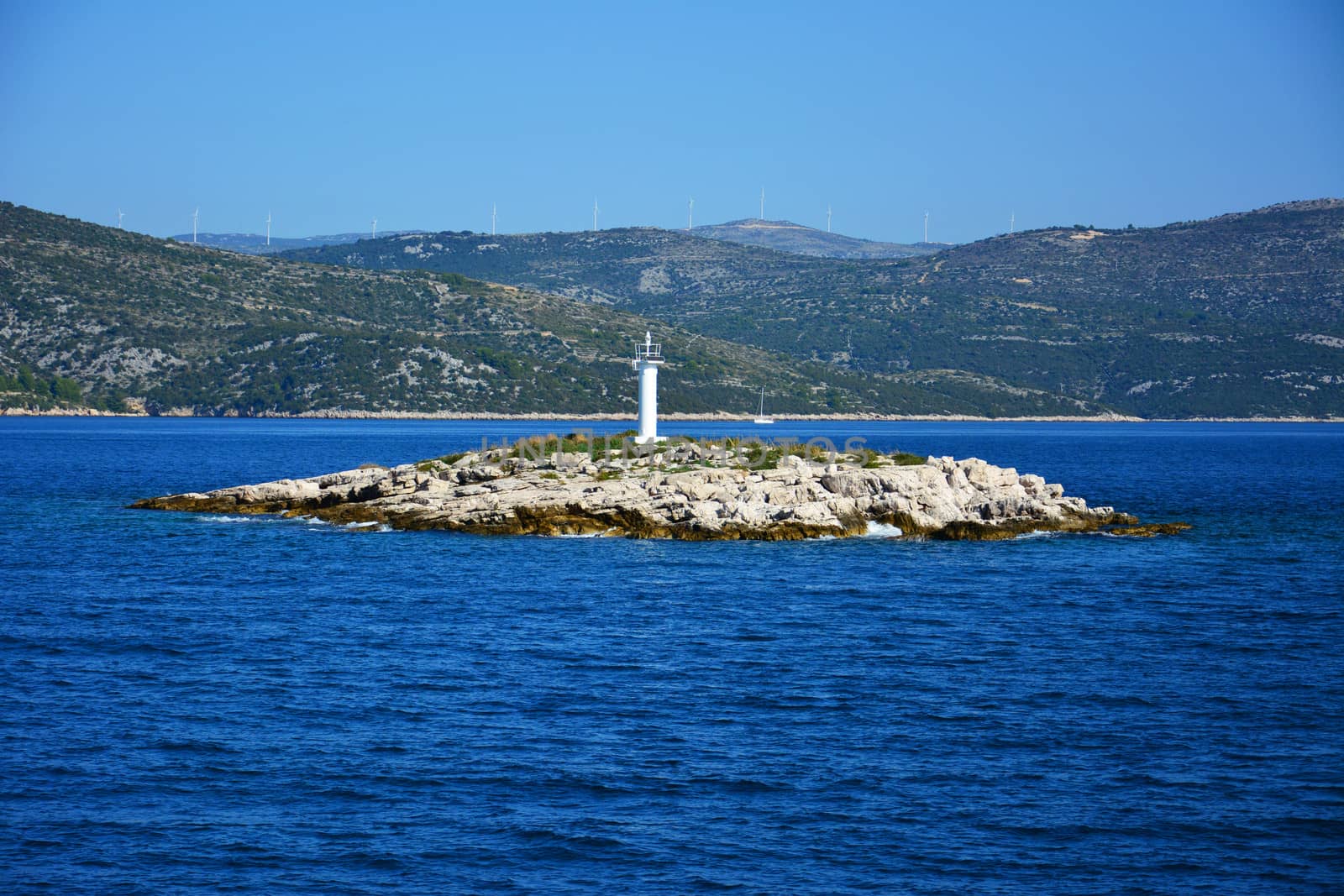 Automatic lighthouse on a small island in Croatia with wind farm in background