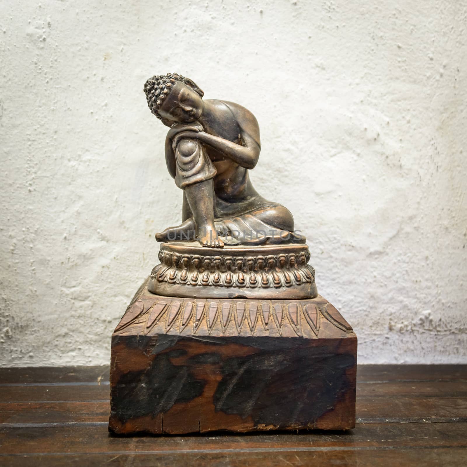 Small wooden Buddha statue, white wall background