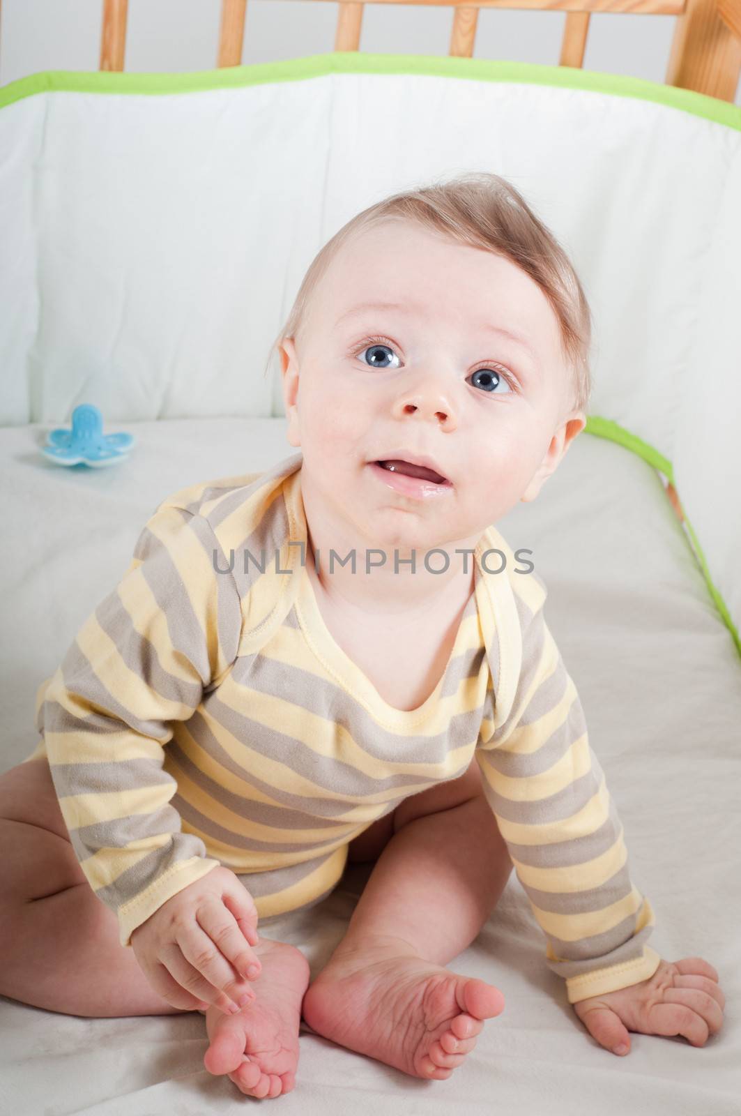 Baby boy in striprd clothes sitting in cradle and looking up