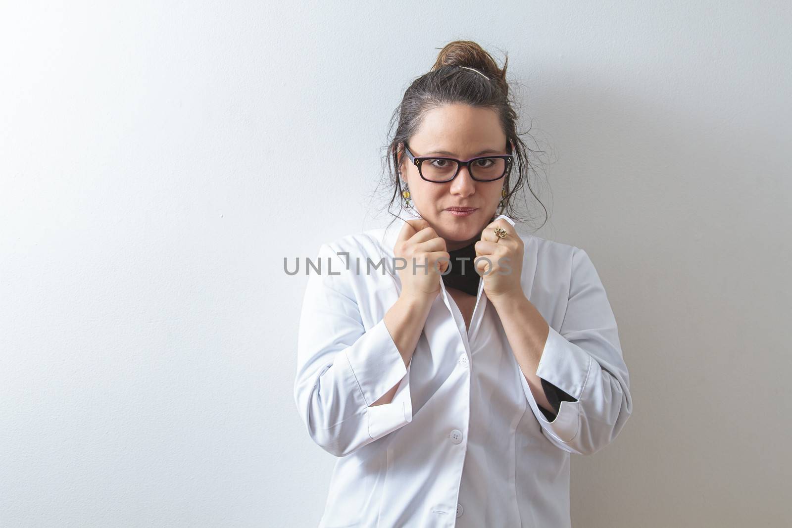 Woman doctor holding up her collar and leaning against a white wall