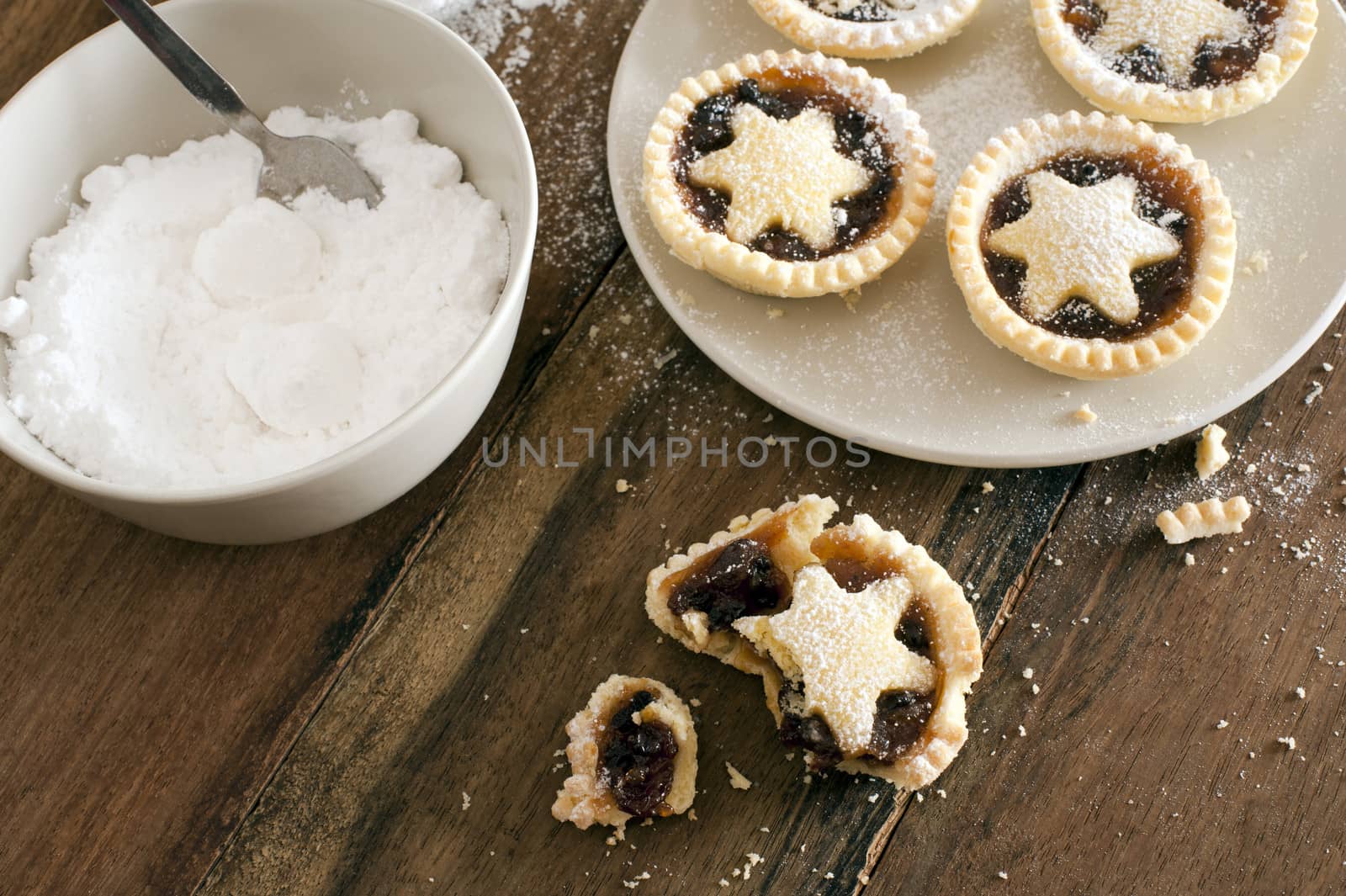 Eating delicious freshly baked Christmas mince pies decorated with pastry stars and sprinkled with icing sugar, one half eaten pie with crumbs in the foreground
