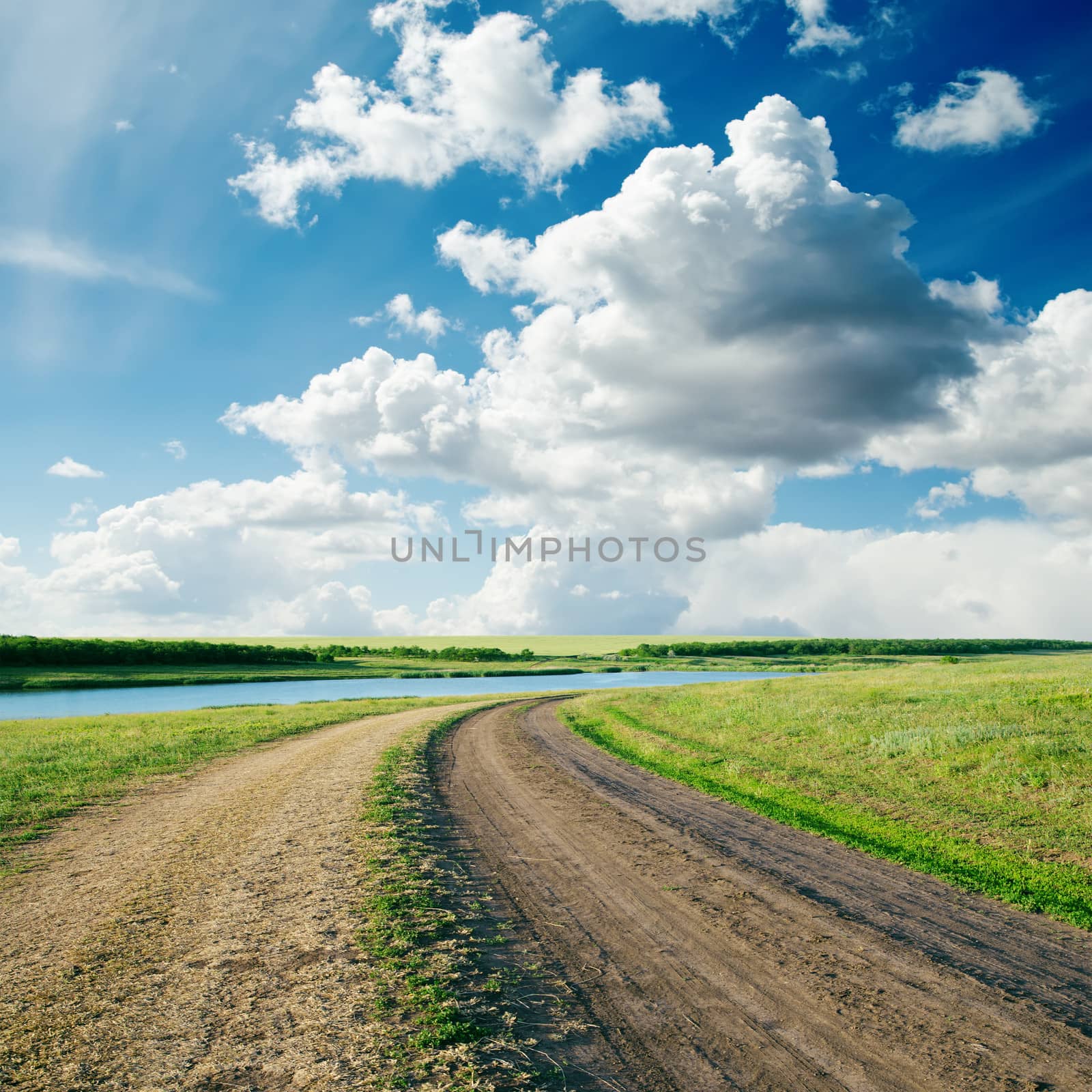 rural road in green grass and cloudy sky by mycola