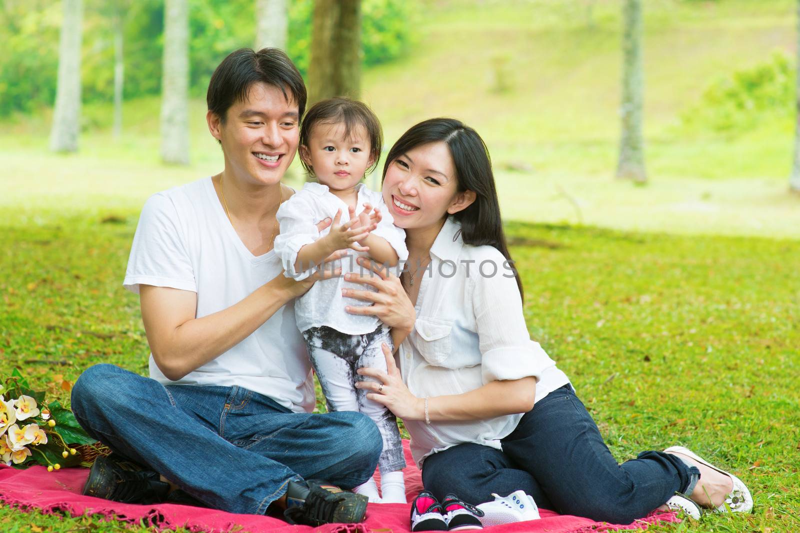 Happy Asian family outdoor activity. Parents and daughter having , picnic on garden green lawn.