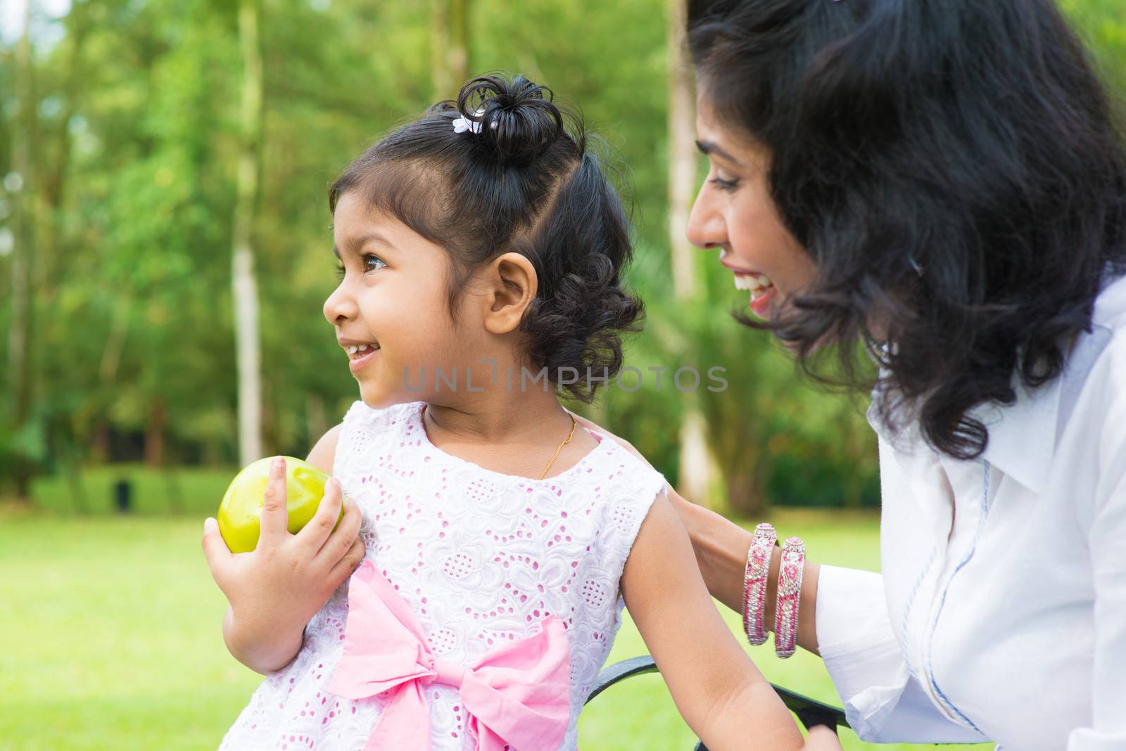 Happy Indian family. Asian girl holding an green apple at outdoor with mother.