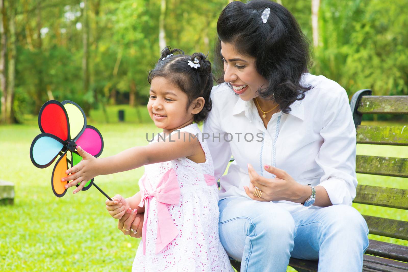 Happy Indian family outdoor activity. Candid portrait of mother and daughter playing windmill at garden park.