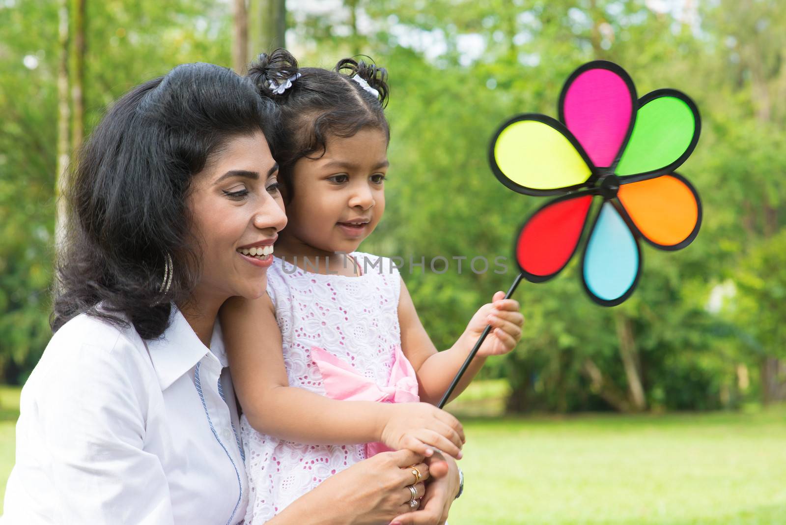 Happy Indian family outdoor activity. Candid portrait of parent and child playing windmill at garden park.