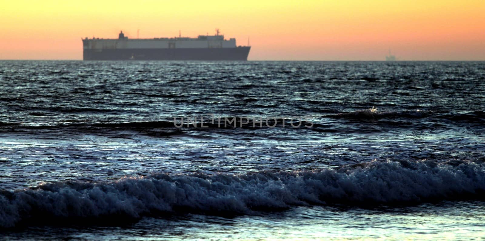 Sunset at a beach with cargo ship in the background.