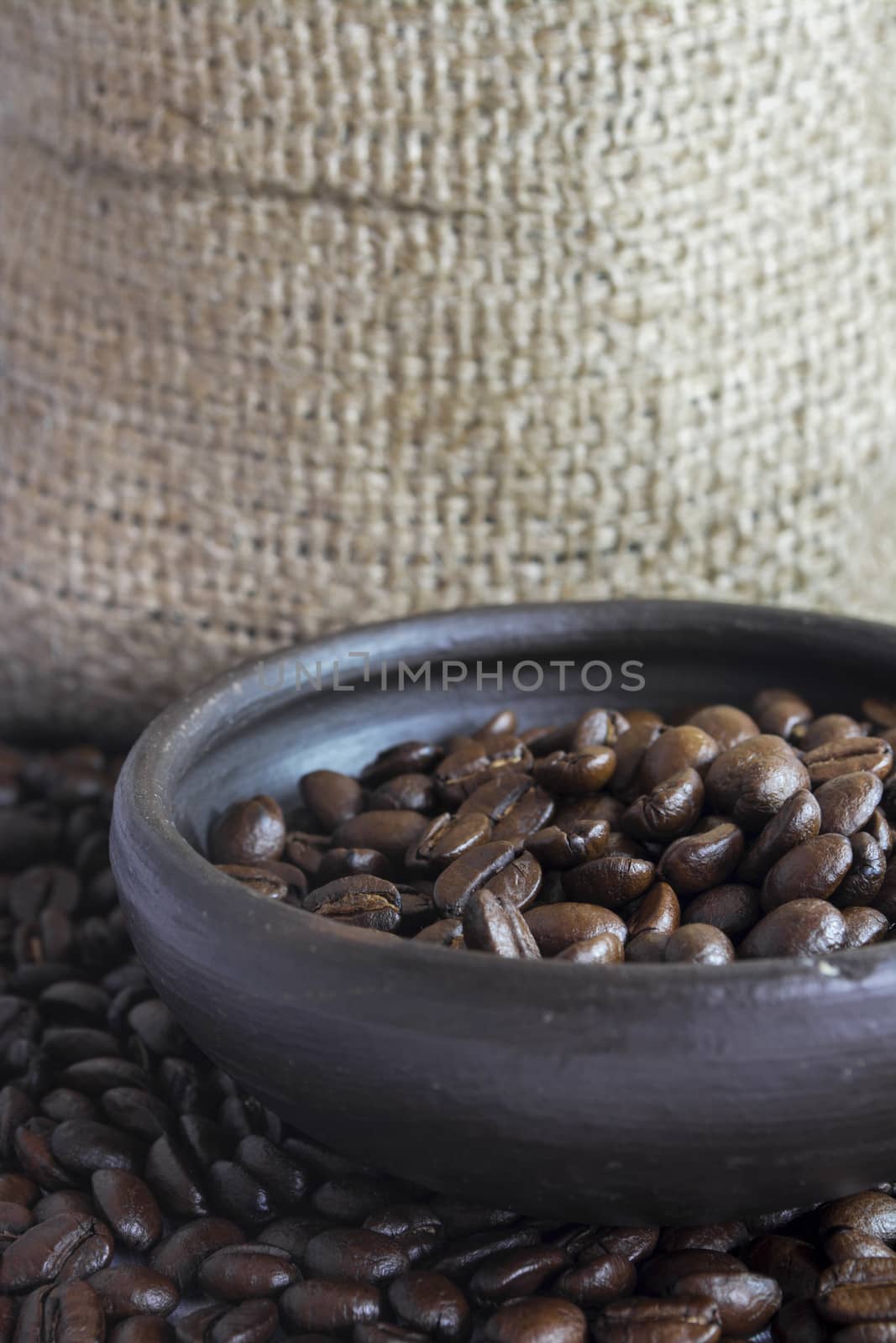 Coffee beans in a small clay pot. Image has a background of jute fibers