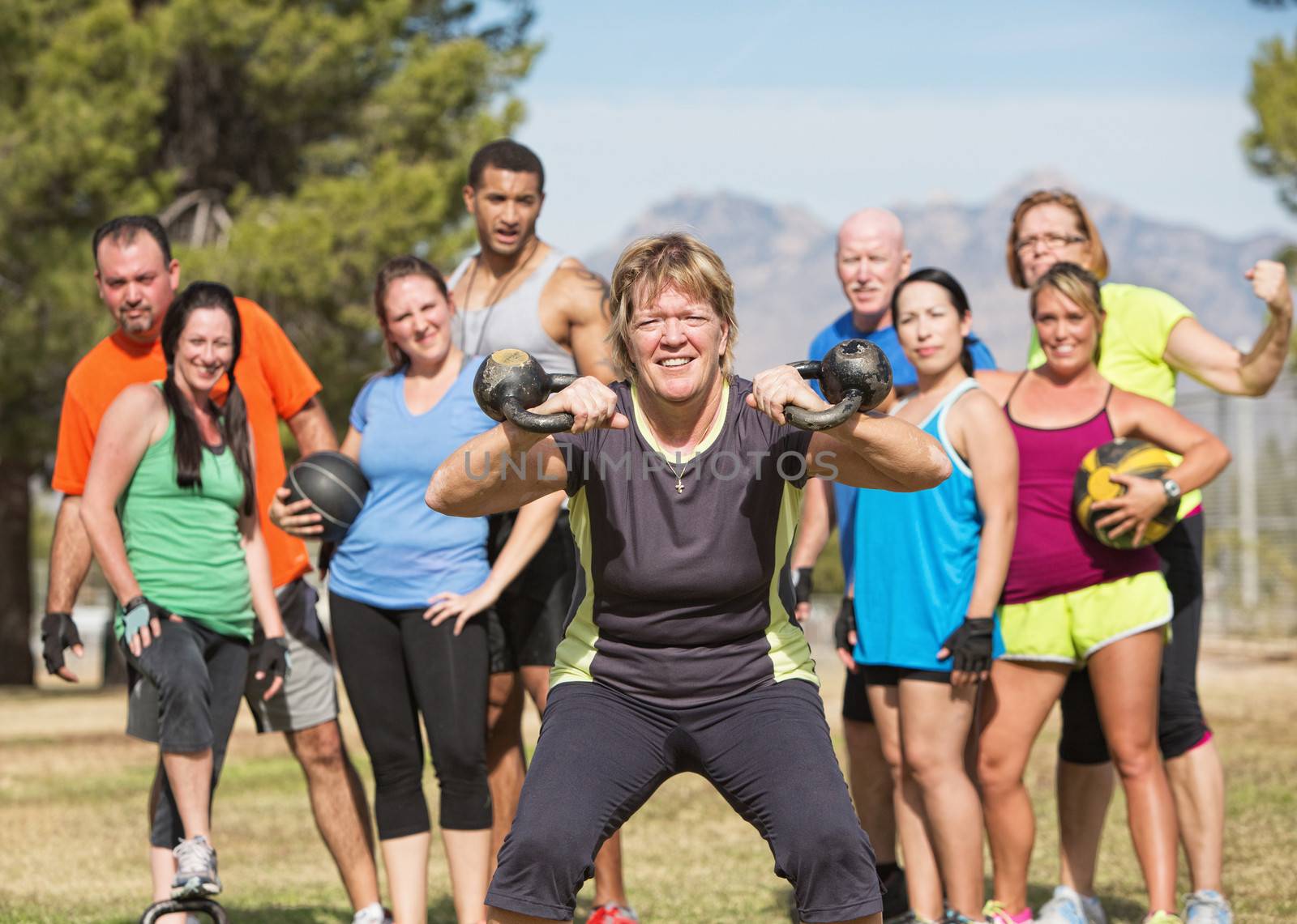 Grinning mature woman lifting kettle bell weights with group