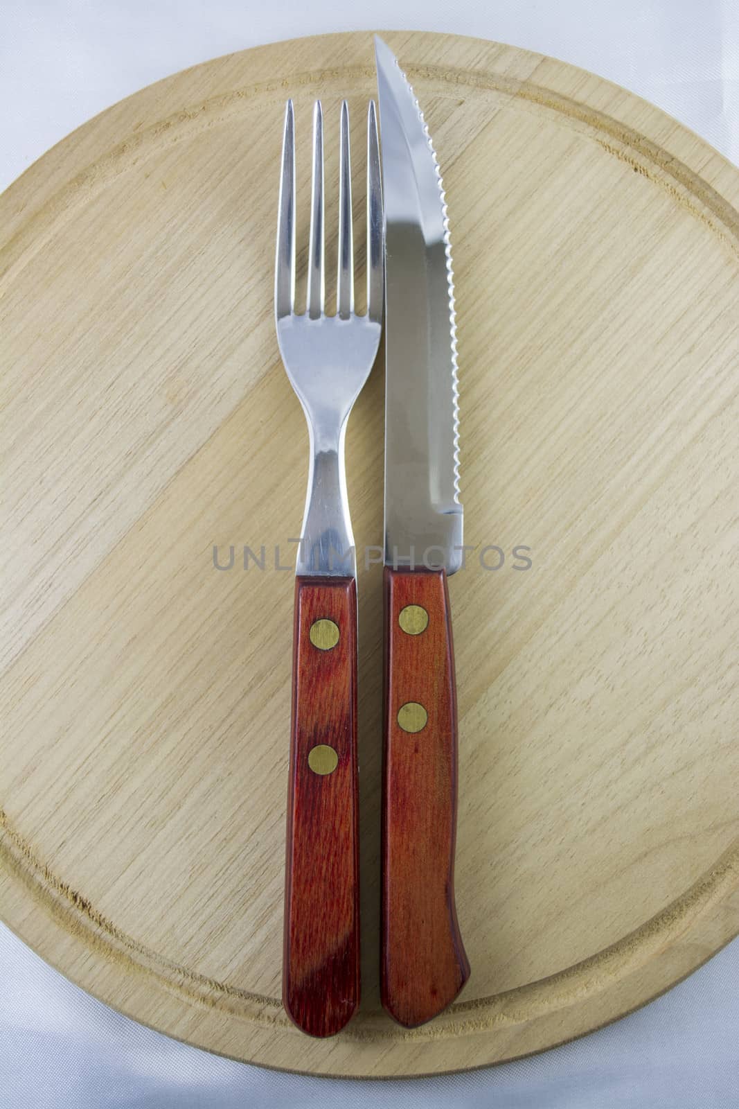 Fork and knife with red wooden handle on a plate of natural wood.
