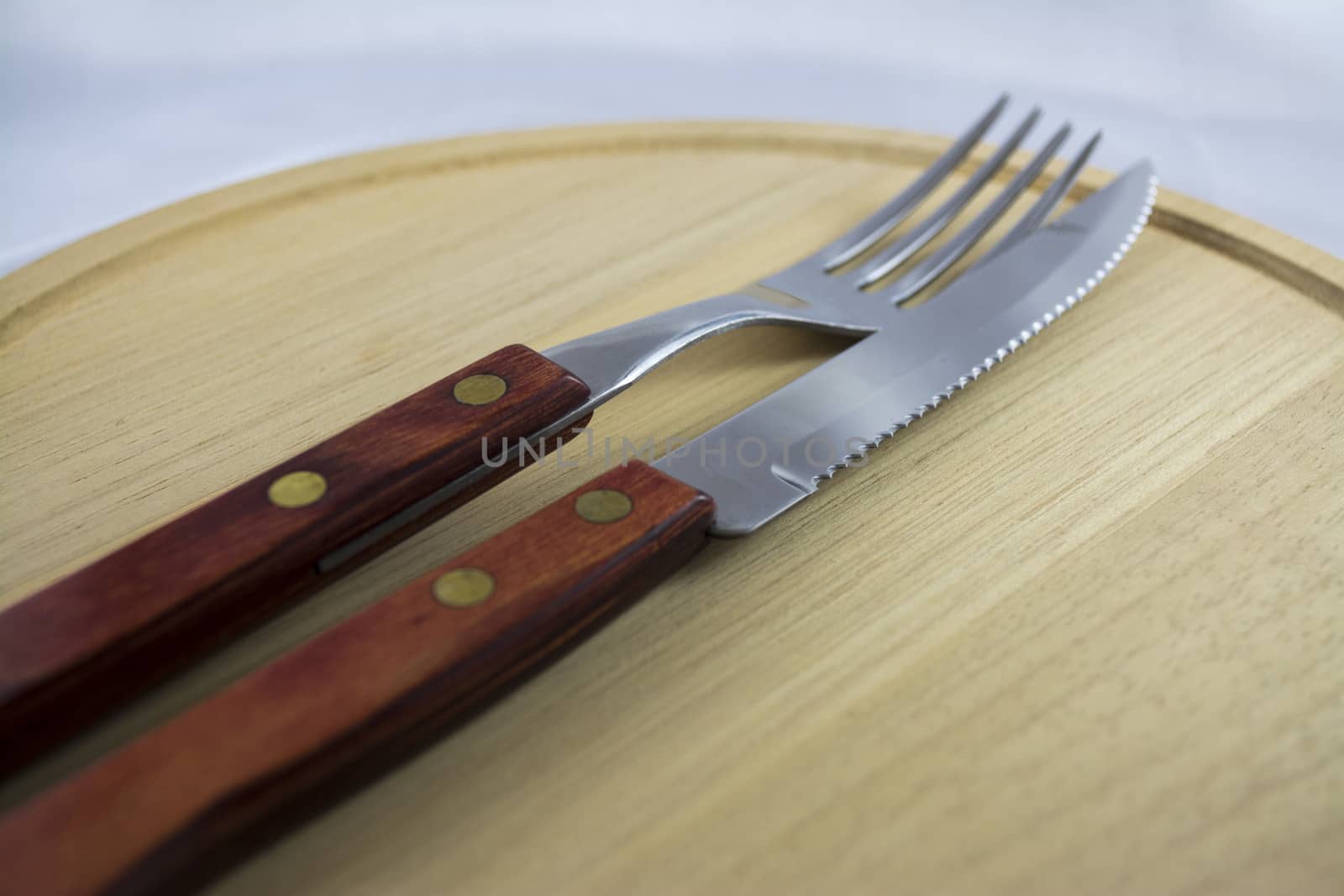 Fork and knife with red wooden handle on a plate of natural wood.