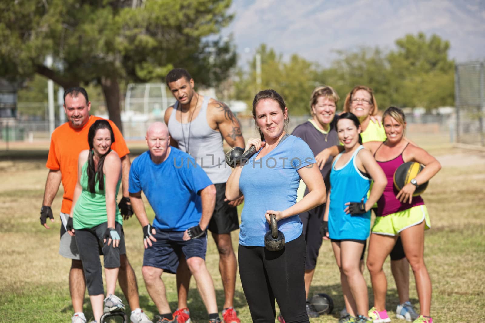Confident young lady with group lifting weights outdoors