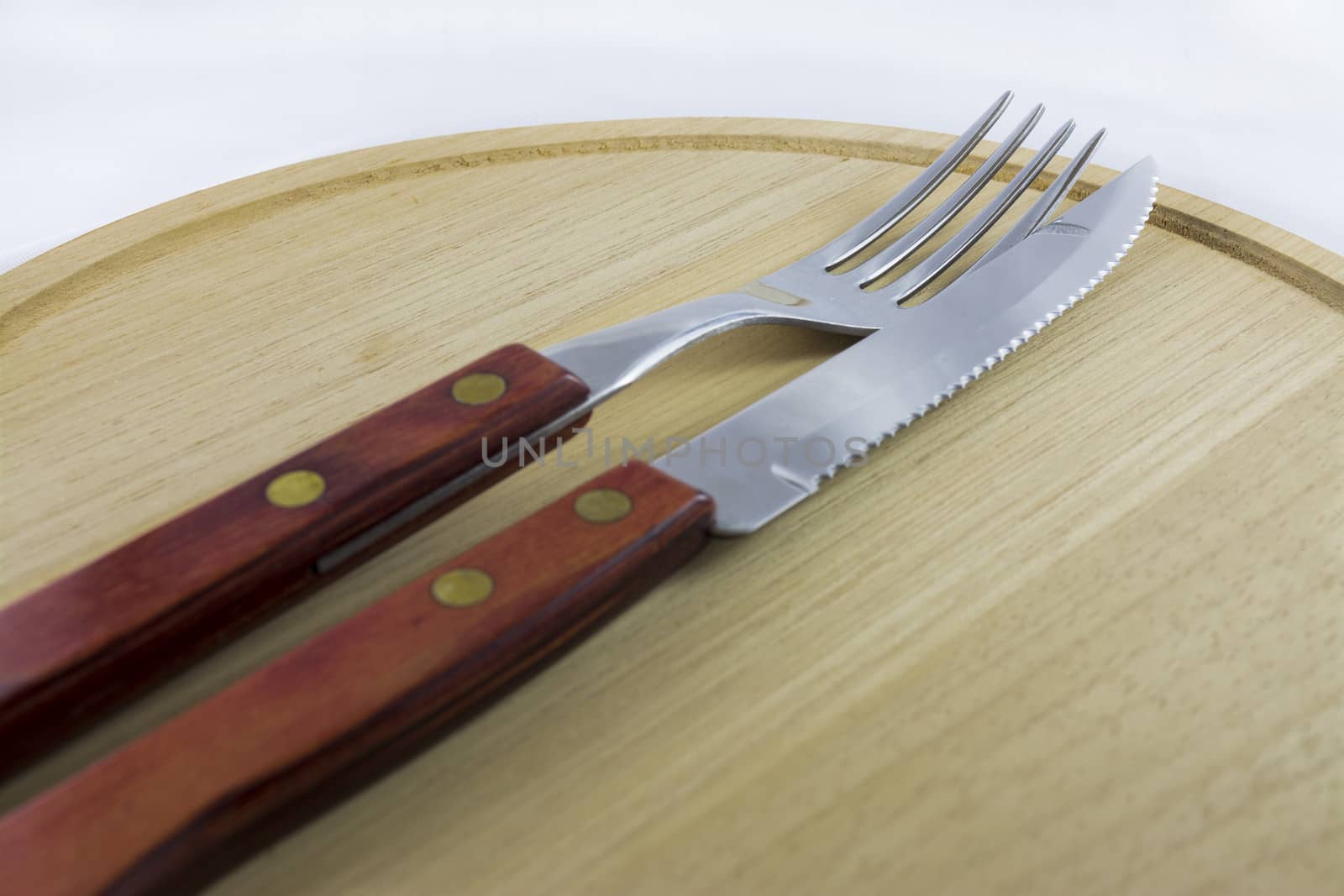Fork and knife with red wooden handle on a plate of natural wood.
