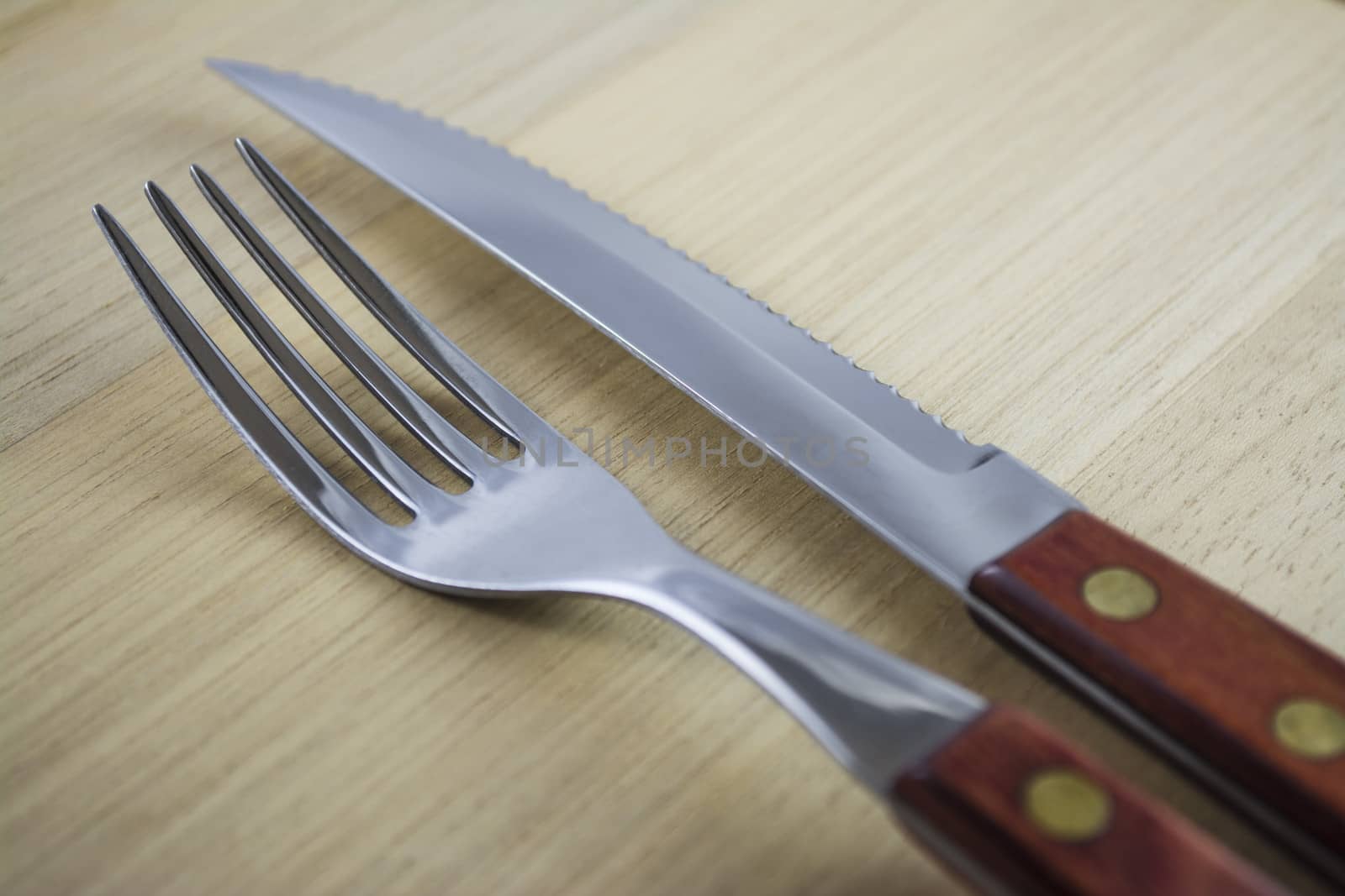 Fork and knife with red wooden handle on a plate of natural wood.