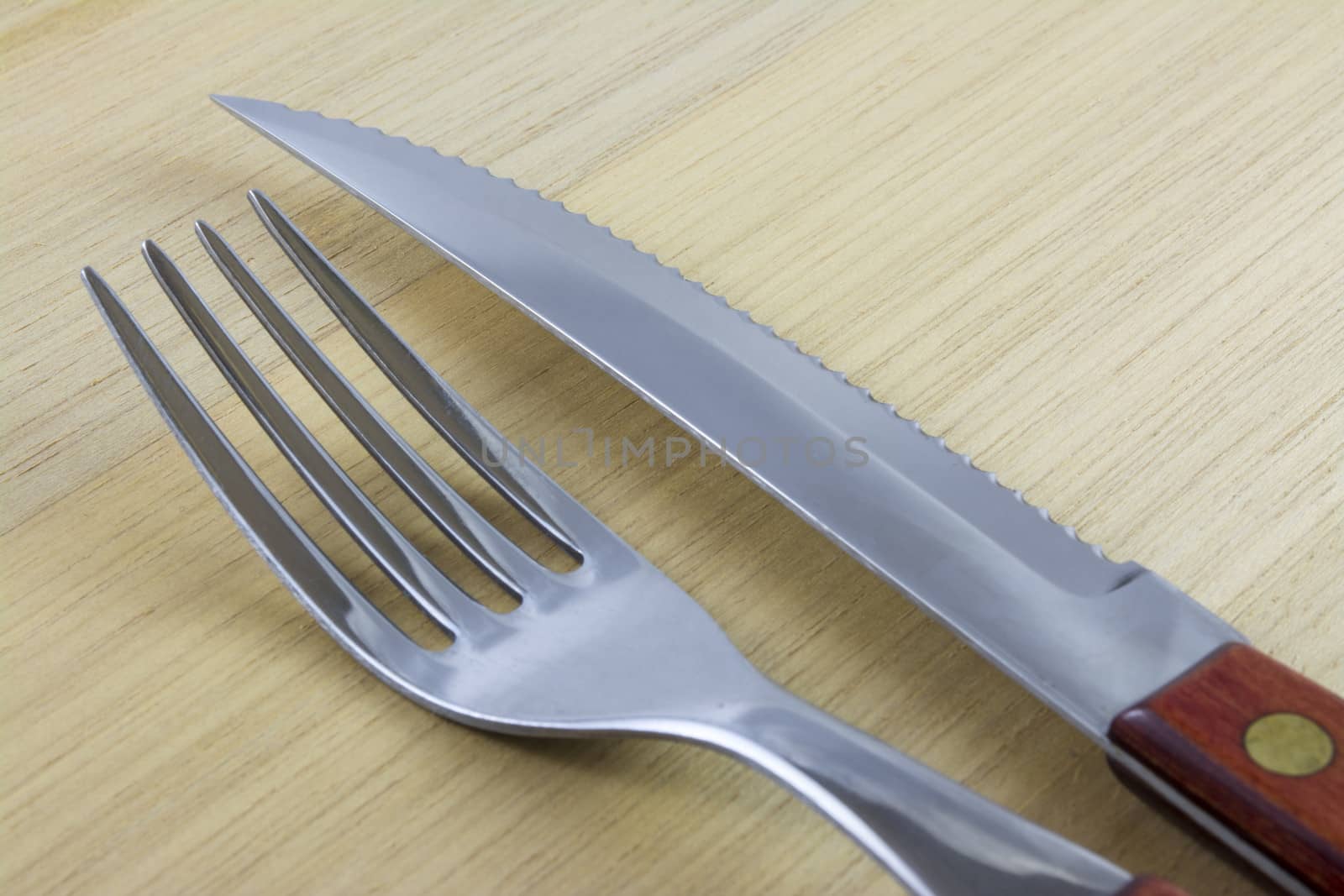 Fork and knife with red wooden handle on a plate of natural wood.
