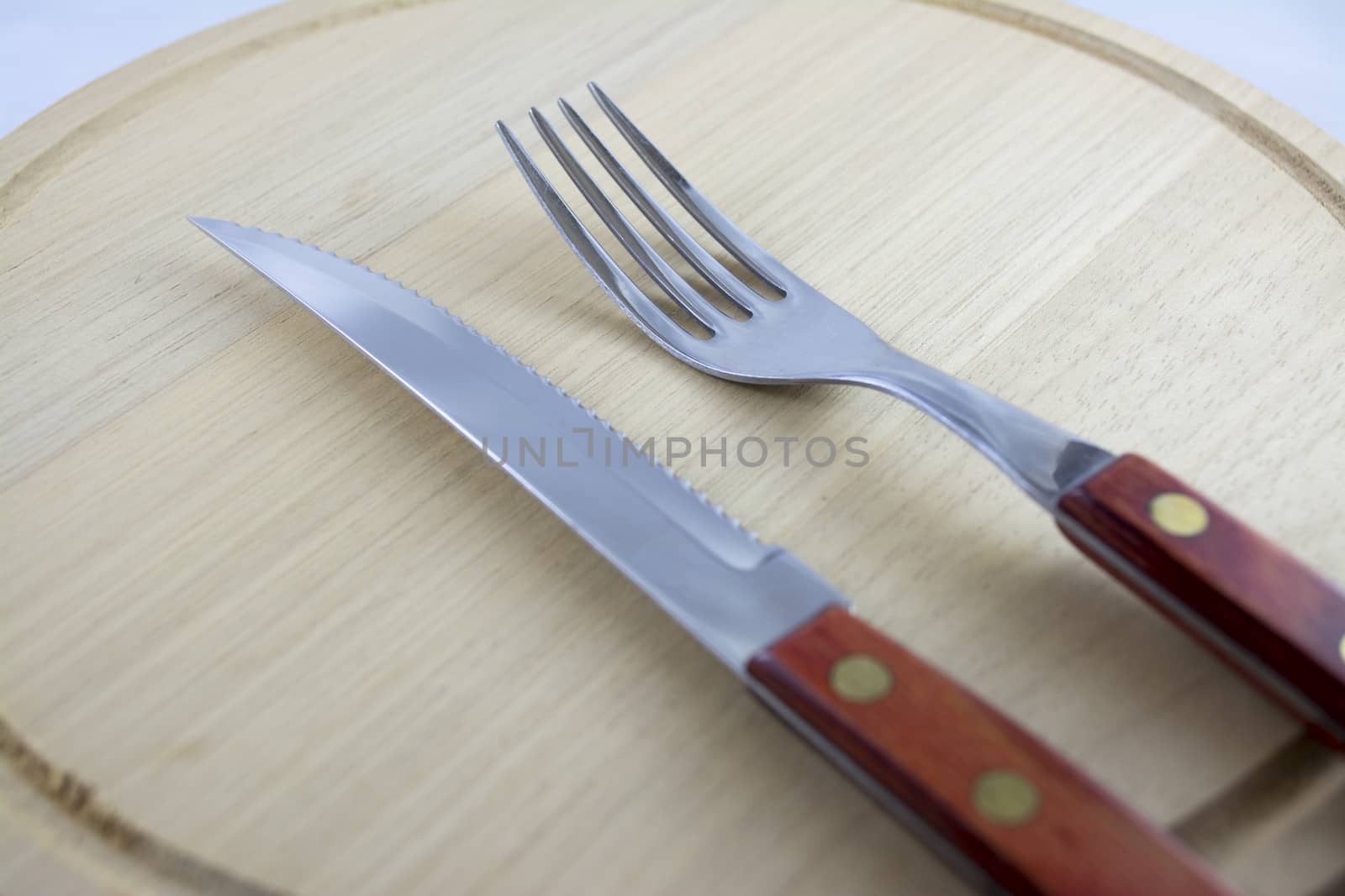 Fork and knife with red wooden handle on a plate of natural wood.
