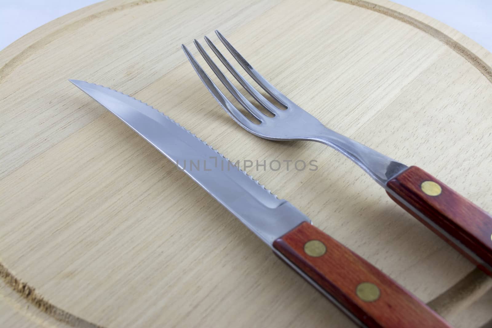 Fork and knife with red wooden handle on a plate of natural wood.