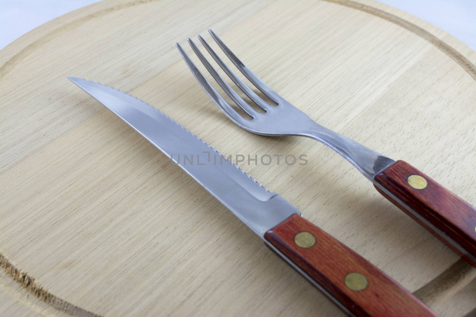 Fork and knife with red wooden handle on a plate of natural wood.