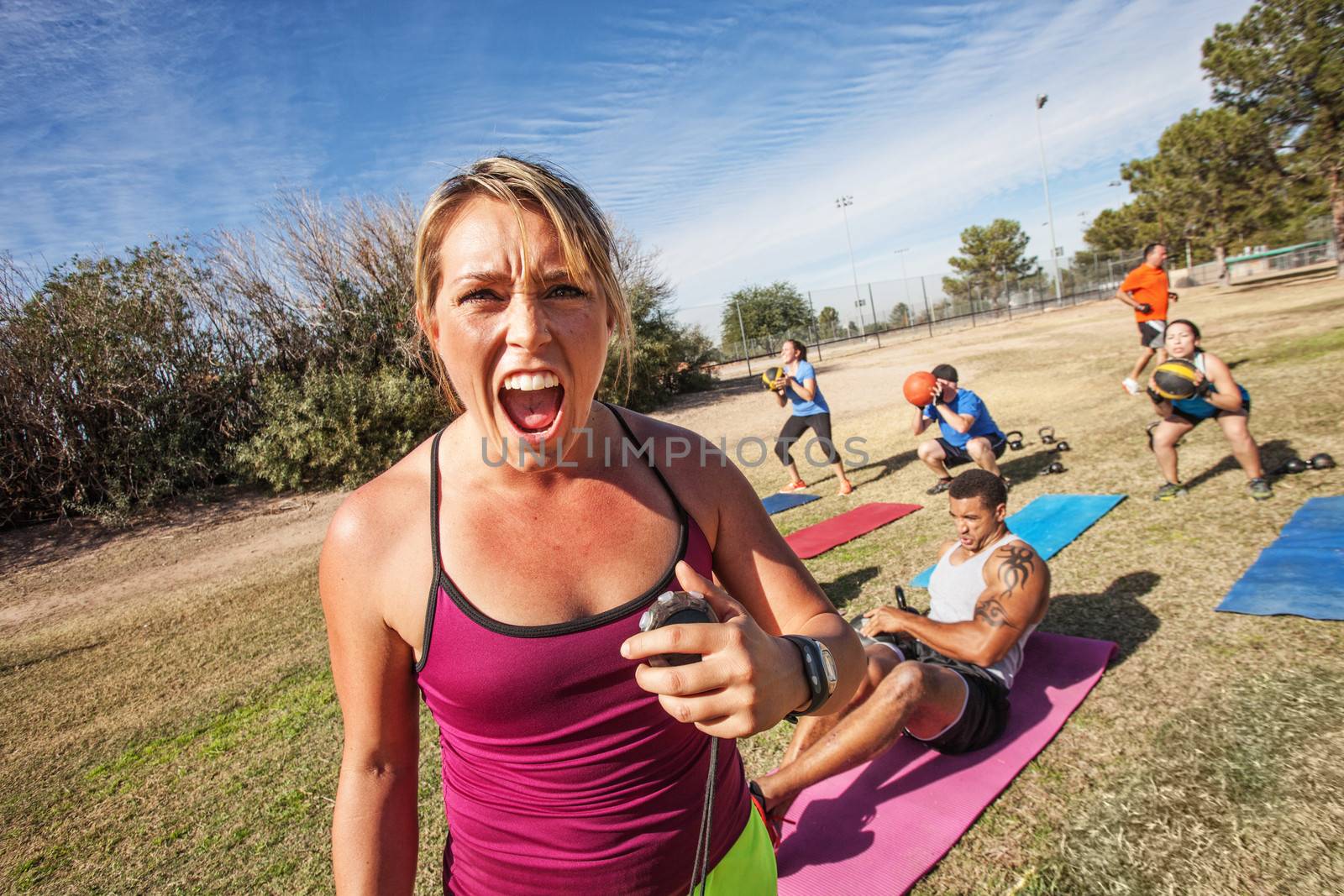 Intimidating boot camp fitness trainer with adult class outdoors