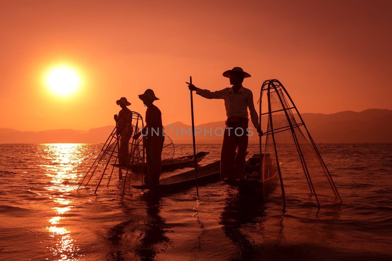 Silhouette of traditional fisherman in wooden boat using a coop-like trap with net to catch fish in Inle lake, Myanmar