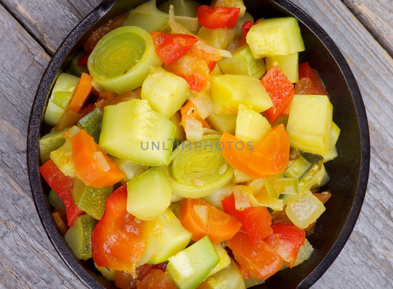 Vegetable Stew with Zucchini in Black Stew Pan closeup on Rustic Wooden background. Top View