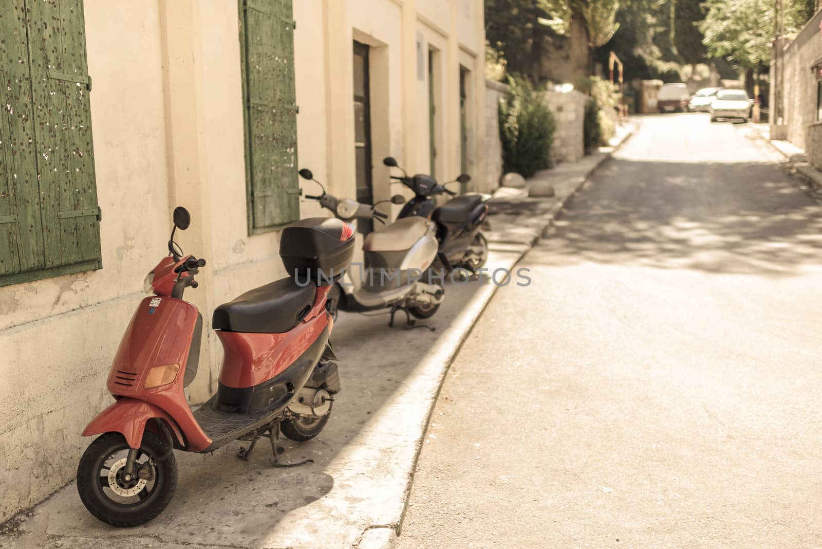 Three scooters parking in empty street in medditaerenian country, visible building with green shutters.