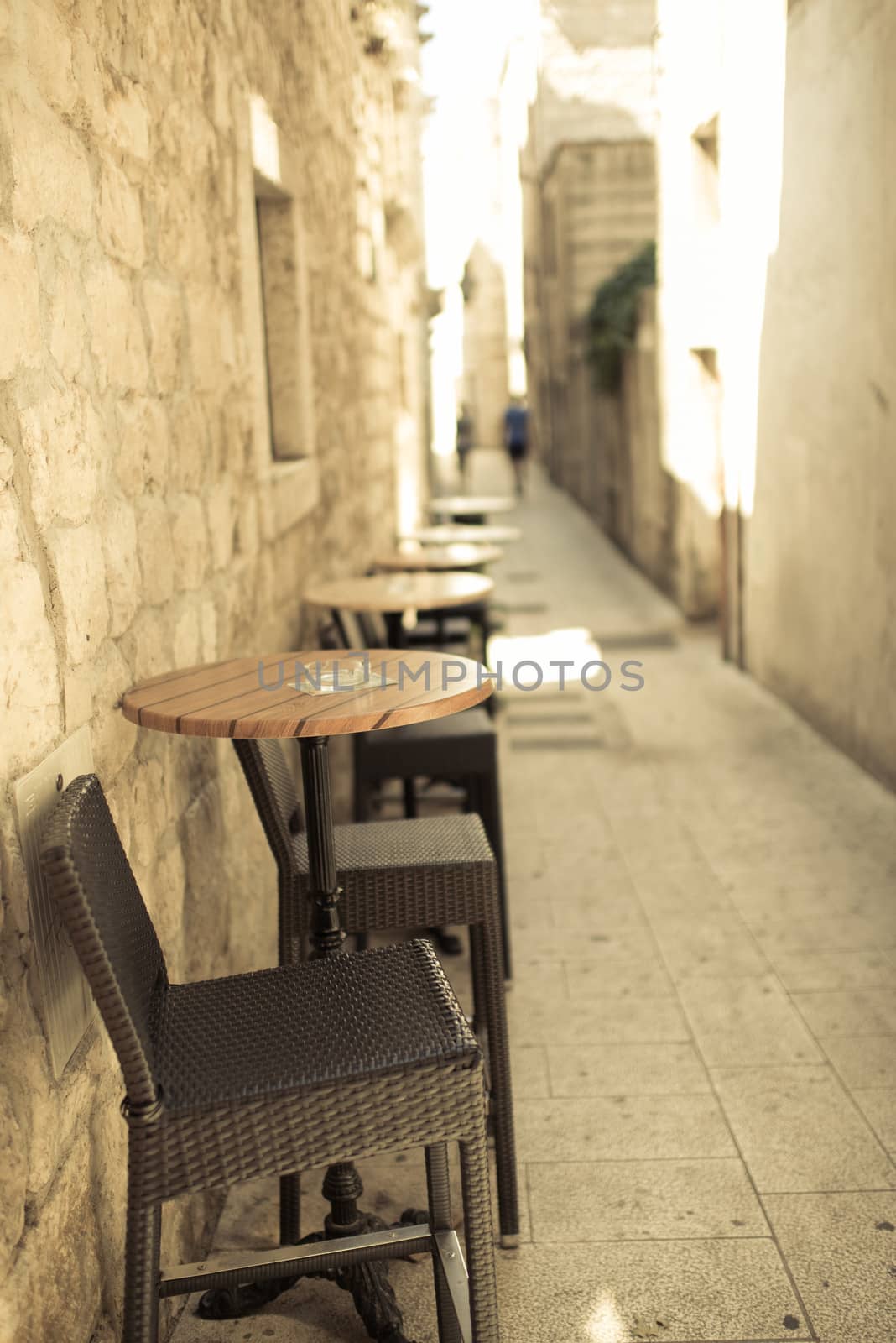 Narrow street of old town with old sandstone buildings, in foreground caffee table and chairs, outdoor photo.