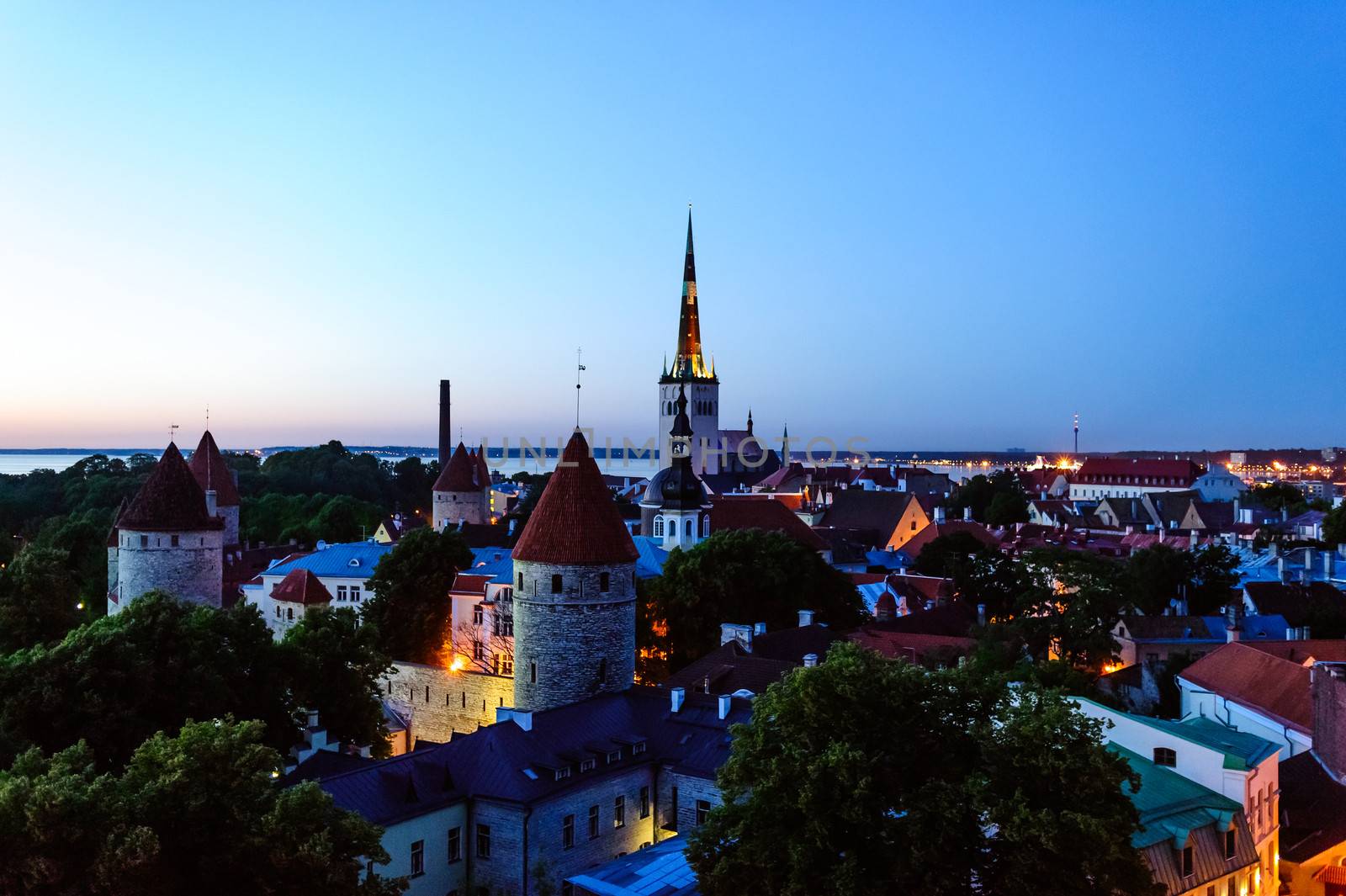 Night photo of old town from top, with clear shapes old church, tower and buildings, visibleillumination in streets, cloudless sky in background.