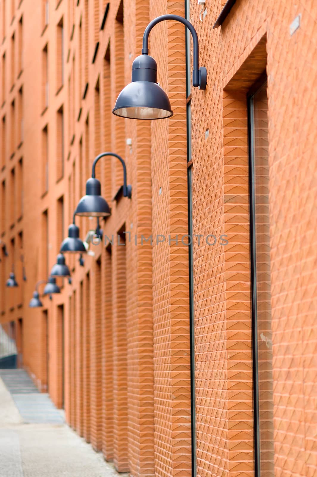 Frontage of modern red brick  building ith visible fragments of windows and black street lamps, linear perspective.