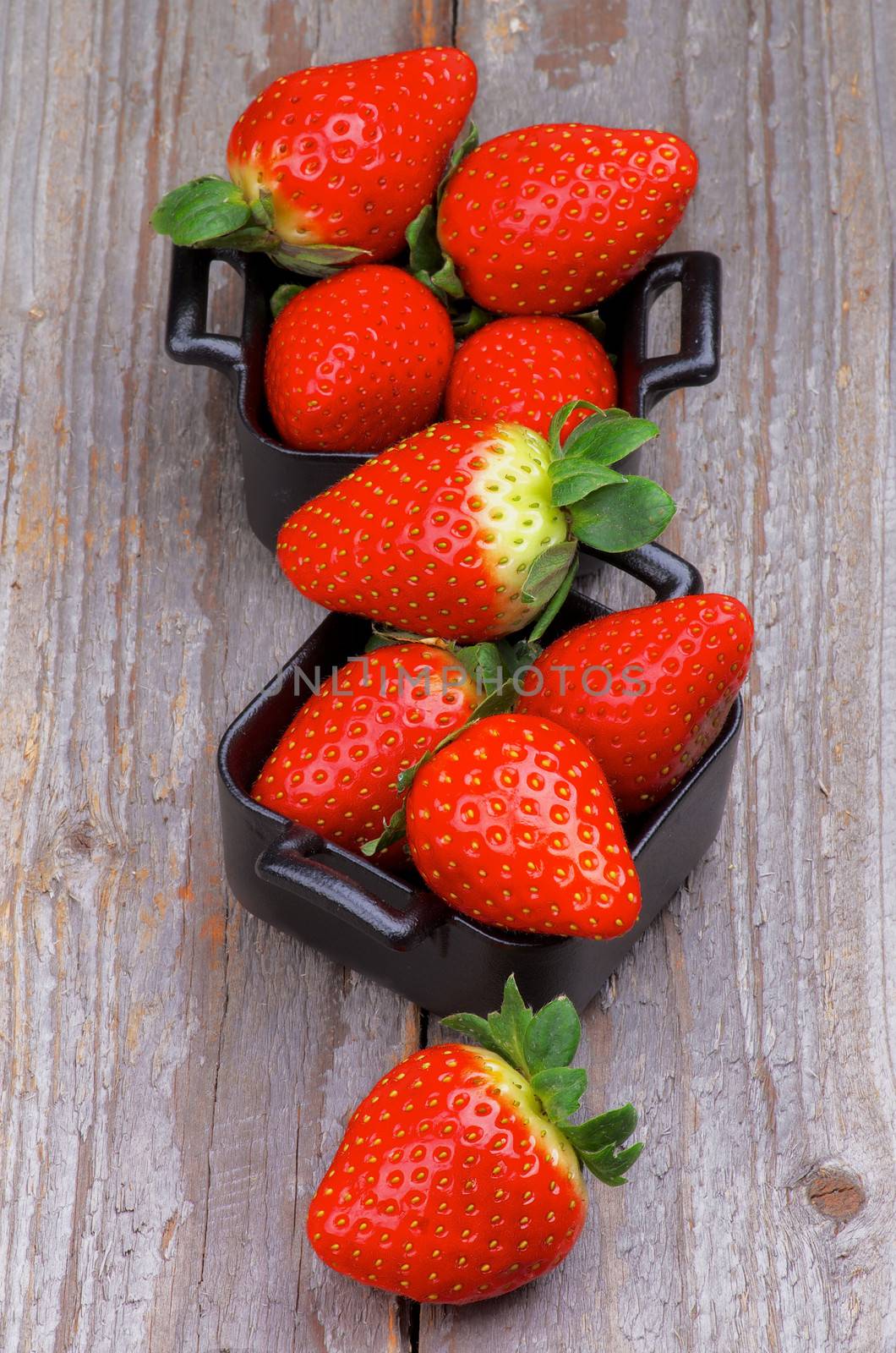 Heap of Perfect Raw Strawberries in Square Shape Black Bowls isolated on Rustic Wooden background