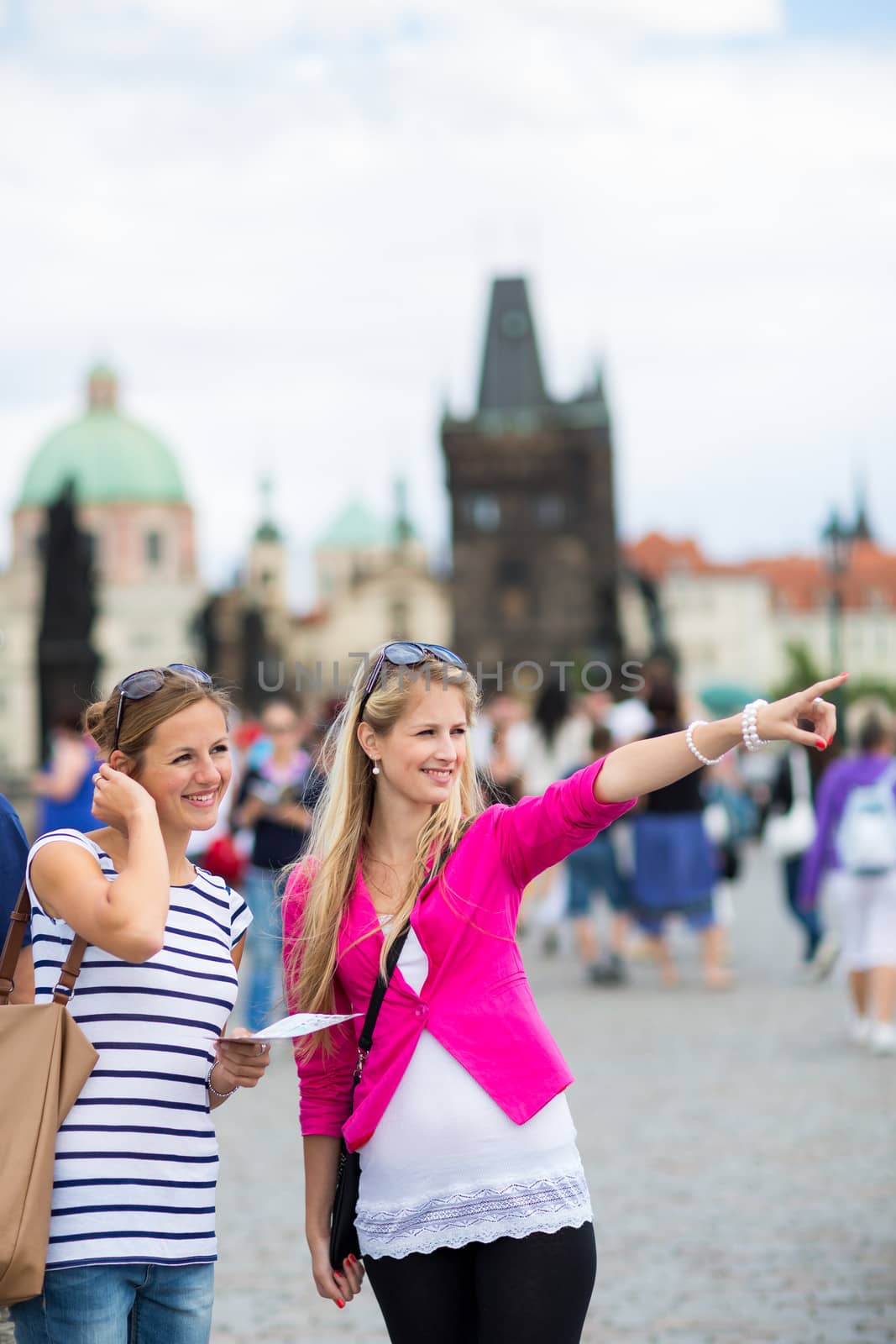 Two female tourists walking along the Charles Bridge while sightseeing in Prague, the historical capital of the Czech Republic
