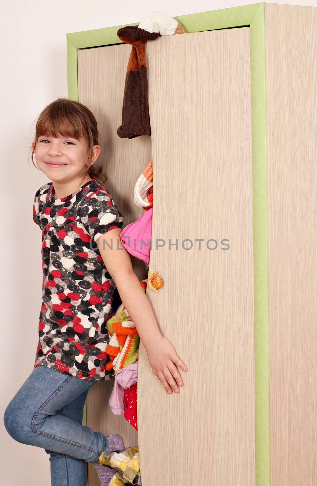 happy little girl trying to close messy closet  by goce