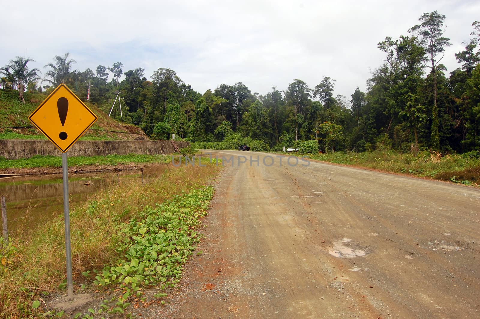 Yellow warning road sign at gravel road rural area, Indonesia