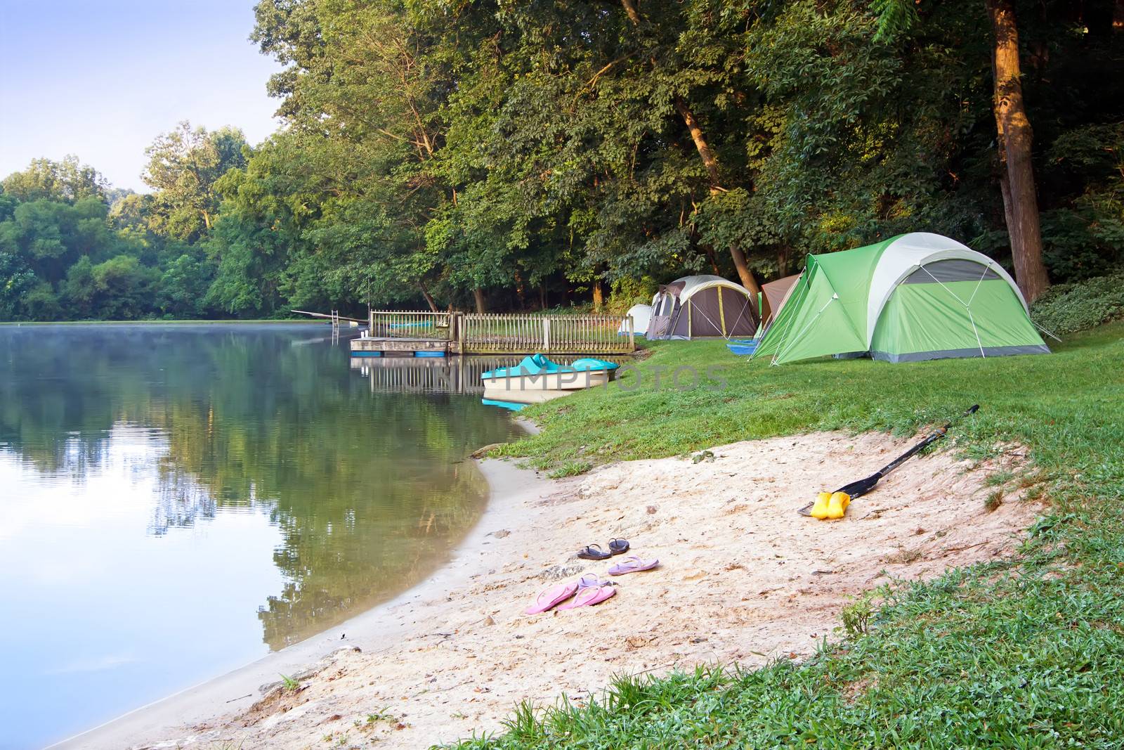 A family campsite at the lake illuminated by early morning sunlight. 