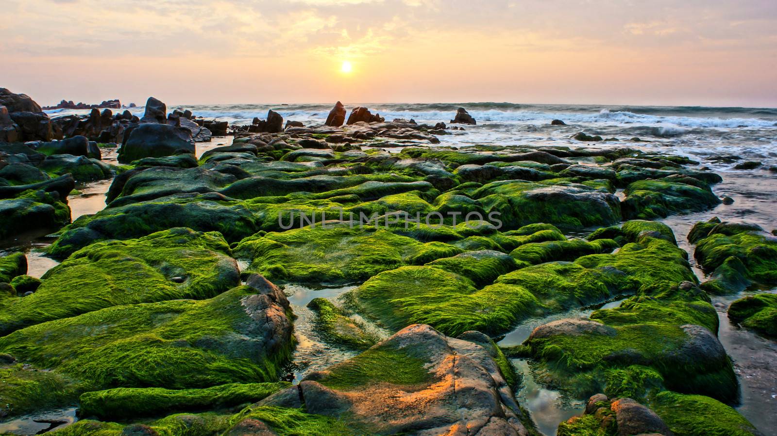 Beautiful, amazing landscape of nature with green moss cover stone, the sun go up at horizon, very white waves surf onto large rock make mysterious, peaceful, impressive scene like paradise on sea 
