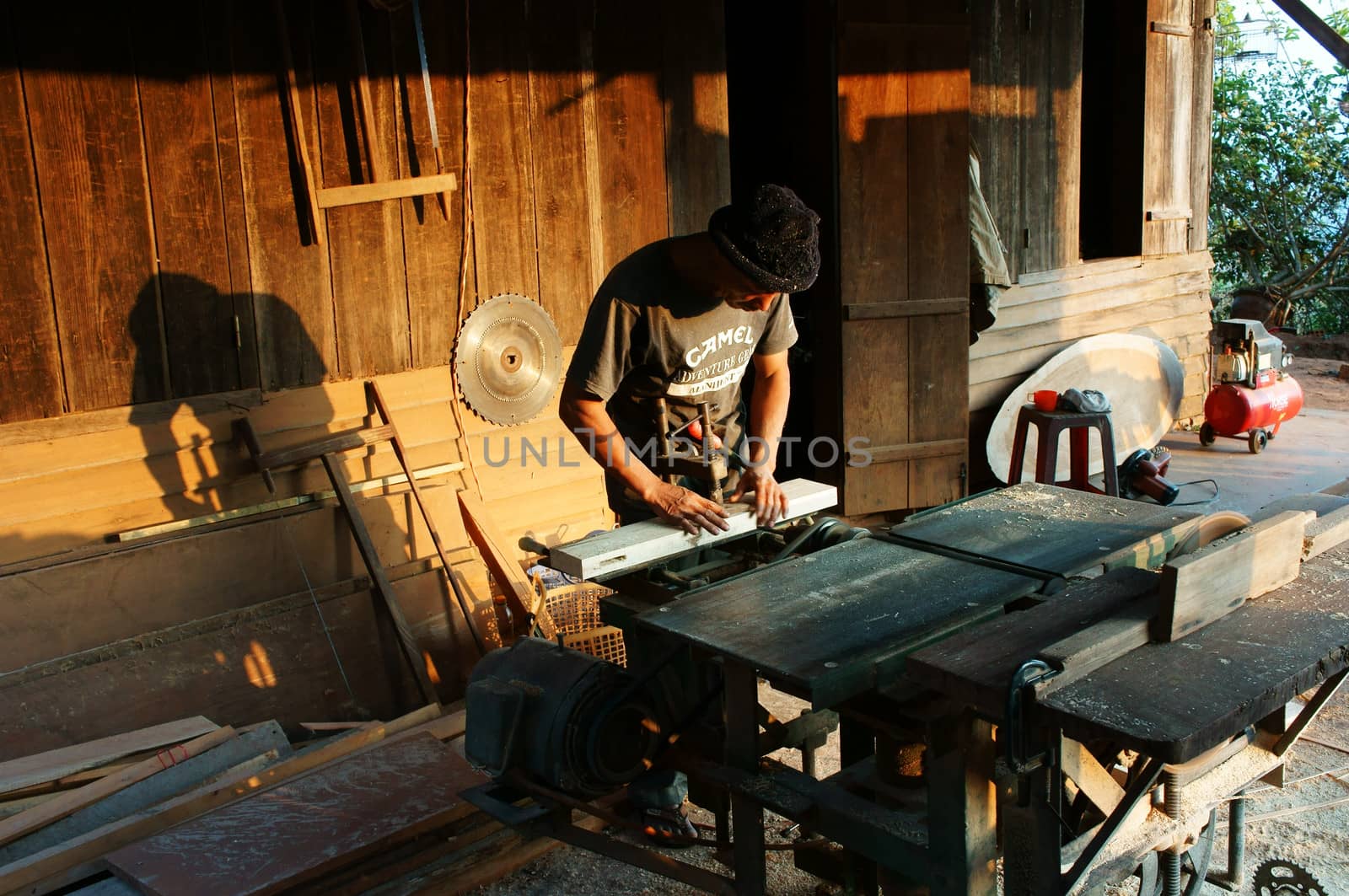 DALAT, VIETNAM- JAN 24: Carpenter saw wood by power saw at home, he working with concentration, his shadow reflect on the wall of wooden house, Viet Nam, Jan 24, 2014                           