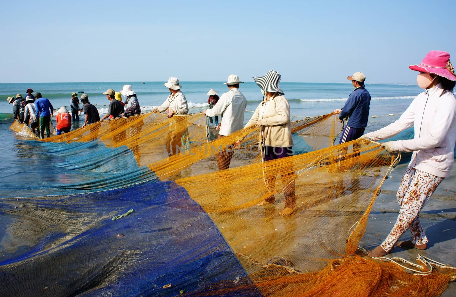 BINH THUAN, VIETNAM- JAN 22: Crowded atmosphere on beach with impression 's group of fisherman pull fish net, row of people with long net in hand, Viet Nam, Jan 22, 2014                            