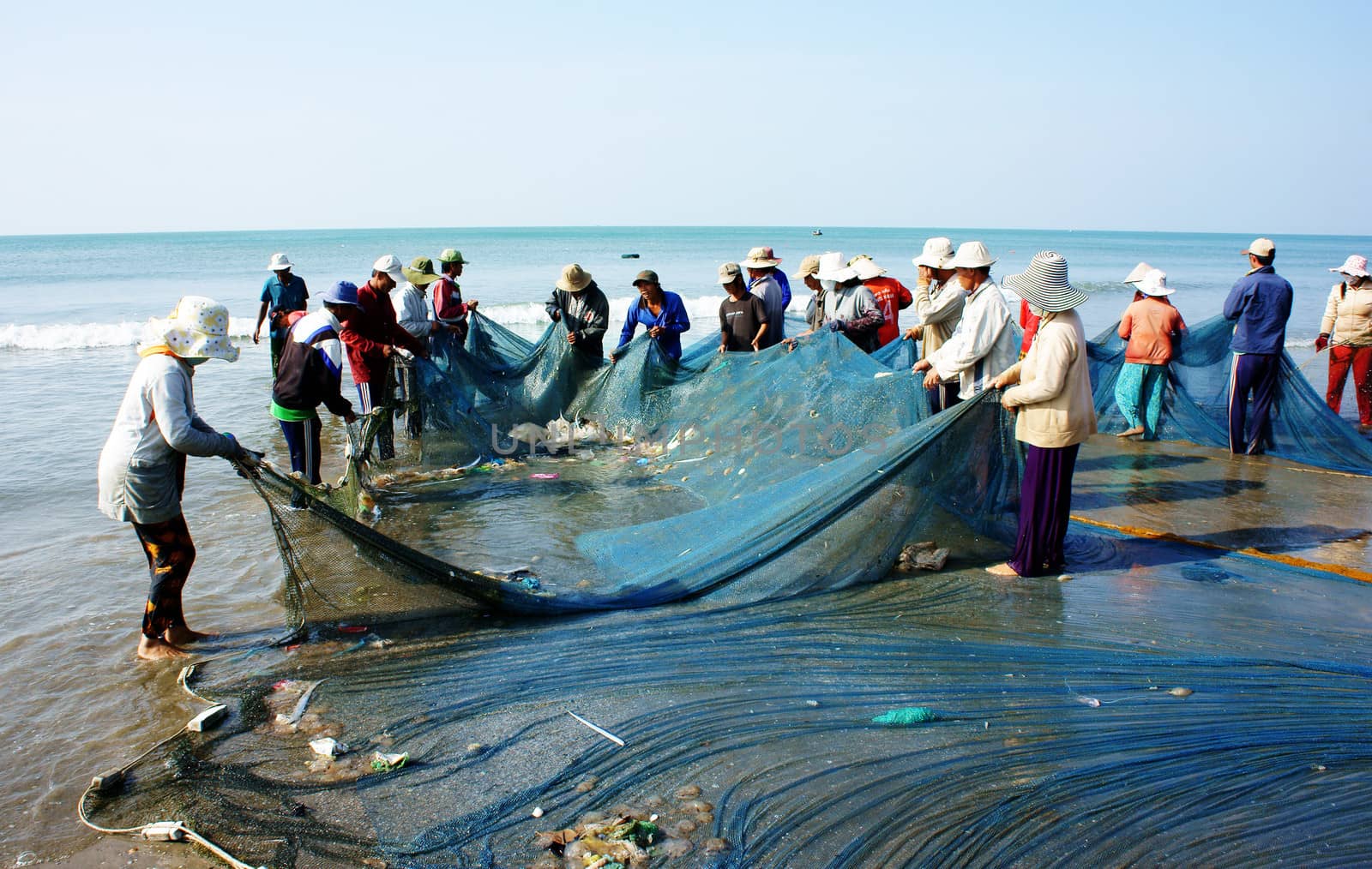 BINH THUAN, VIETNAM- JAN 22: Crowded atmosphere on beach with impression 's group of fisherman pull fish net, row of people with long net in hand, Viet Nam, Jan 22, 2014                         