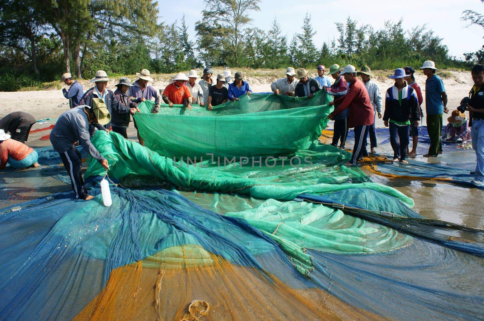 BINH THUAN, VIETNAM- JAN 22: Crowded atmosphere on beach with impression 's group of fisherman pull fish net, row of people with long net in hand, Viet Nam, Jan 22, 2014                           