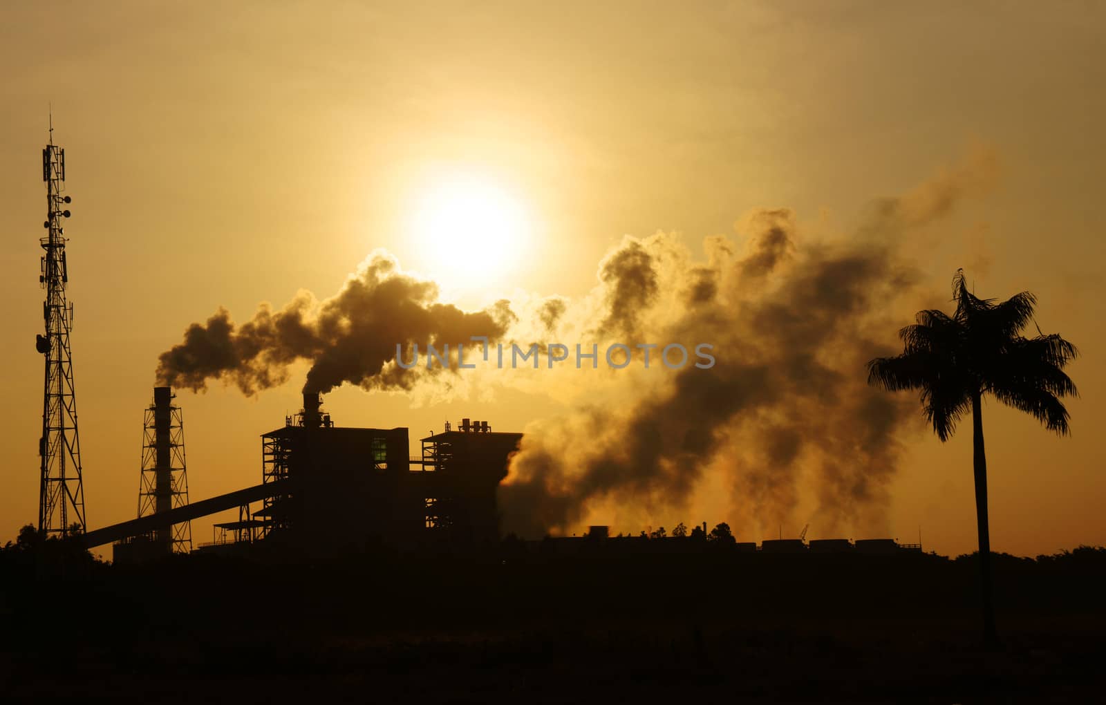 Black smoke from smoke stack of factory in industrial zone rose in to the air, it make polluted enviroment, the plant and tree in silhouette at sunrise, atmosphere cover with waste exhaust
