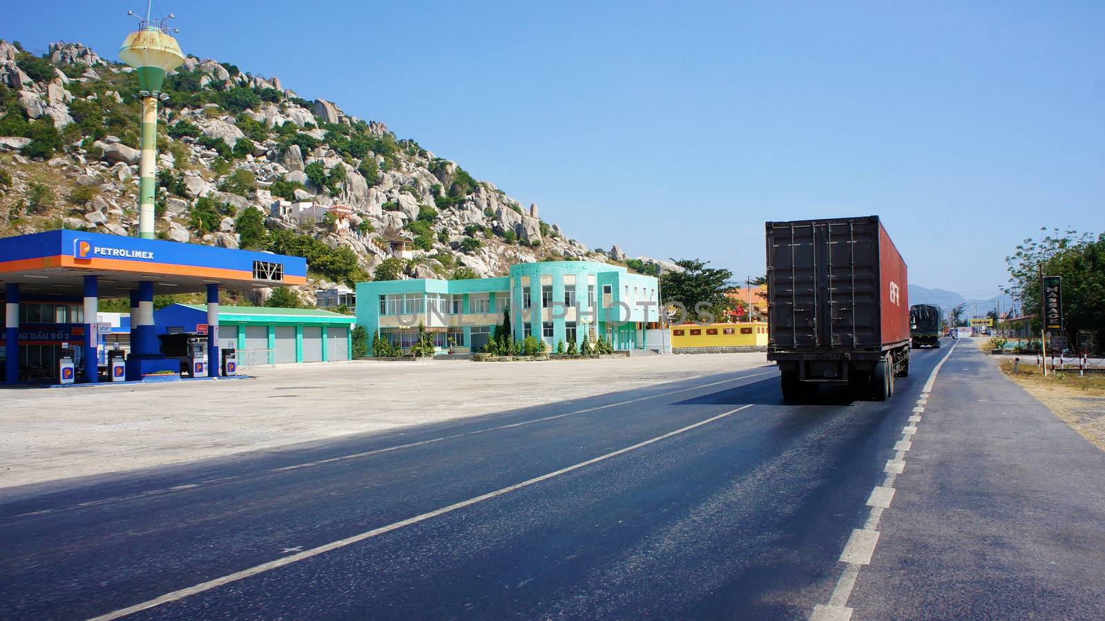 NINH THUAN, VIETNAM- JAN 22: Traffic of transport vehicle on highway 1A, the asphalt road and gas station beside impressive mountain under blue sky, truck  moving on day, Viet Nam, Jan 22, 2014