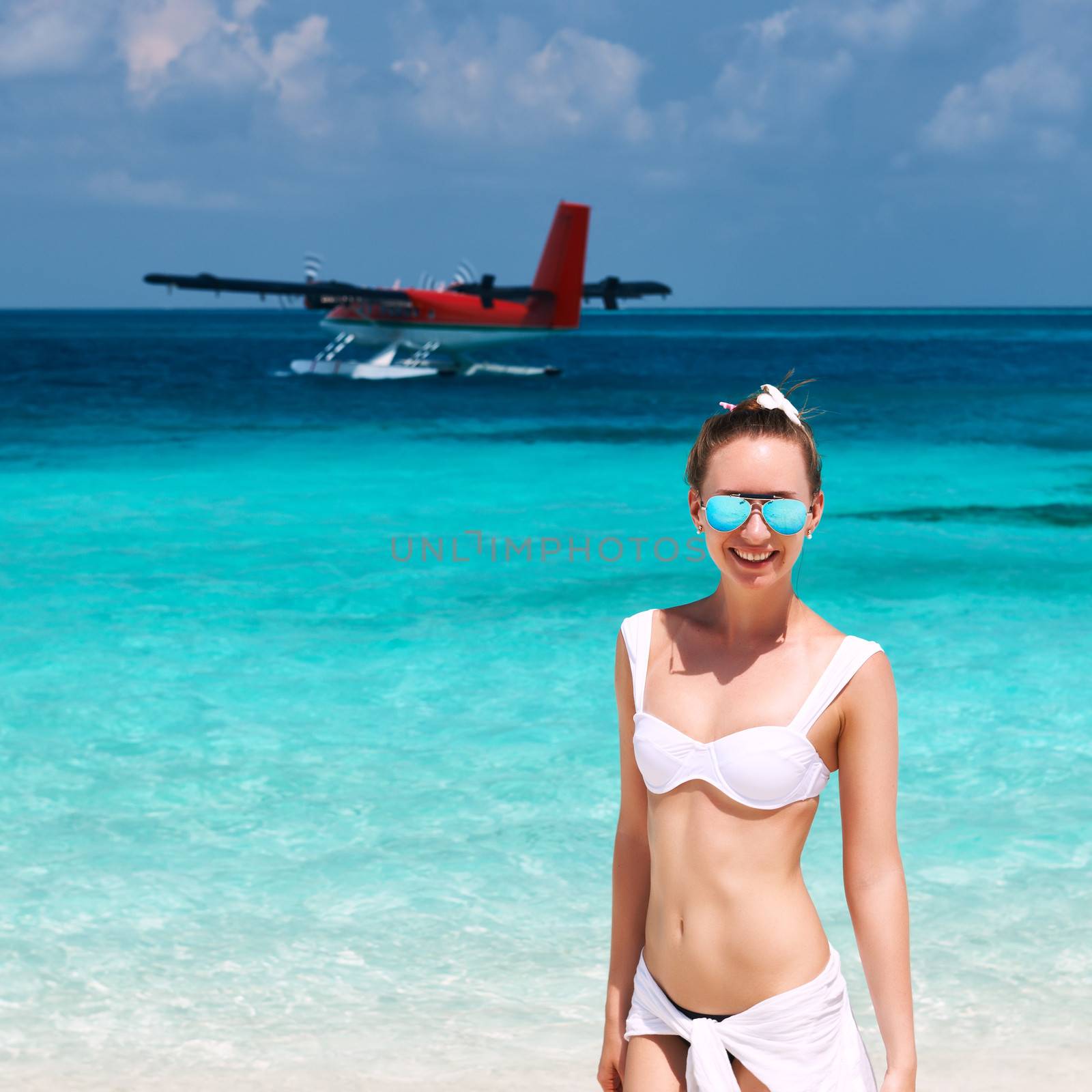 Woman in bikini at tropical beach. Seaplane at background.