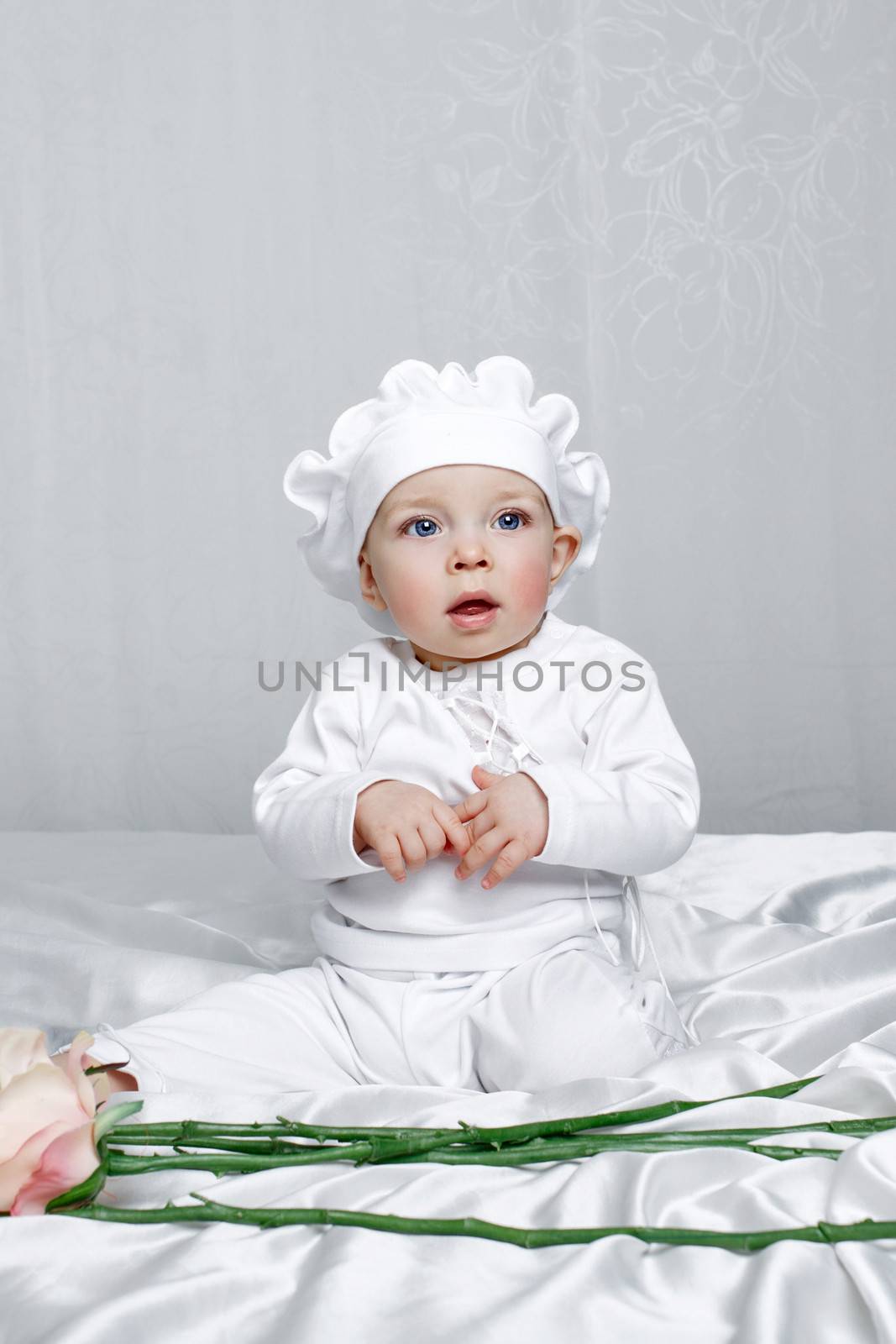 Little girl sitting on silk sheets lie at the feet of flowers