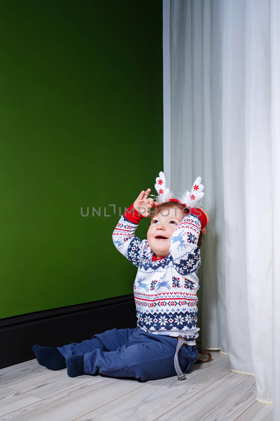 Little boy in a sweater and jeans at home on a wooden floor